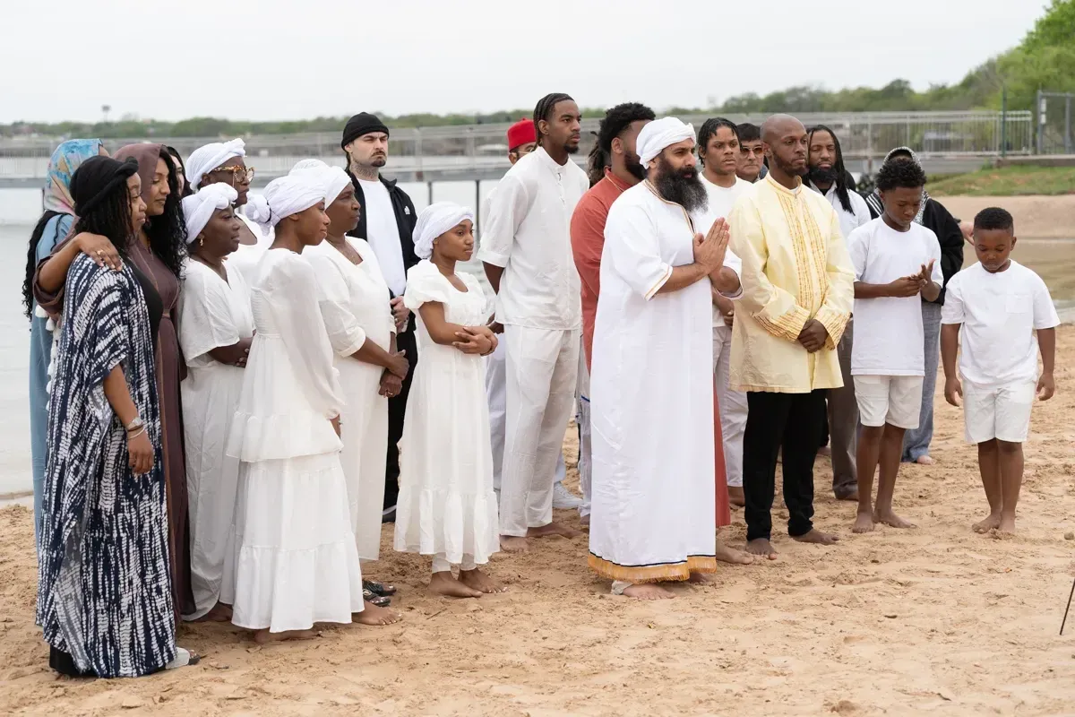 Members of the congregation in white gathered on a beach for immersions.