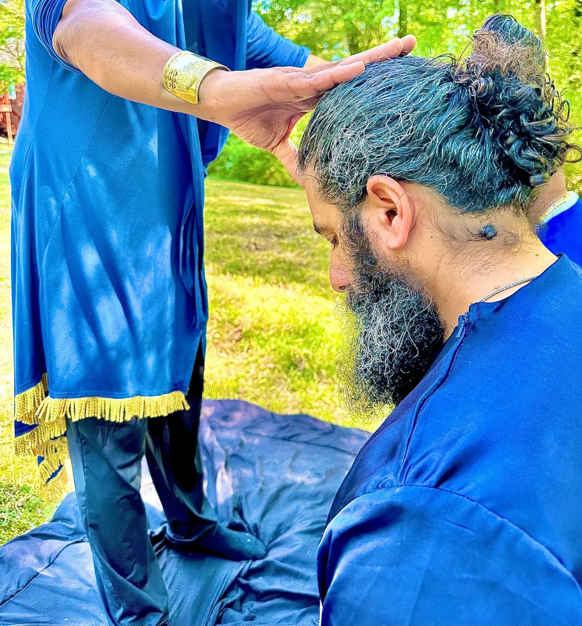 A man kneels with bowed head as a hand rests on his head in anointing.