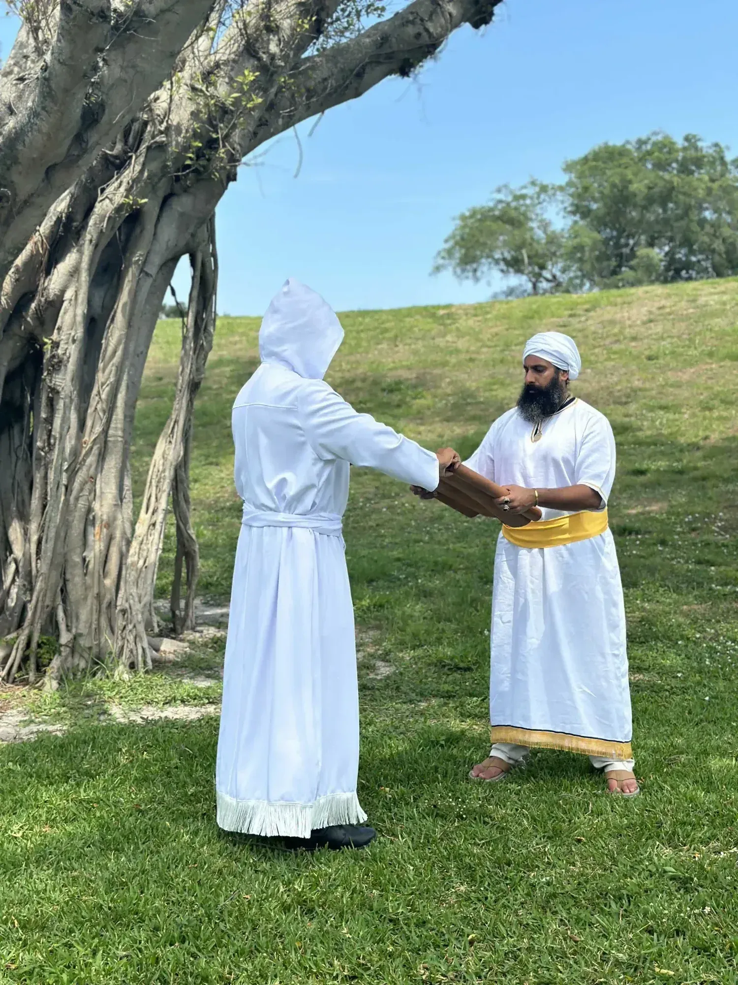 Two men in white robes exchange a scroll beneath a great tree.
